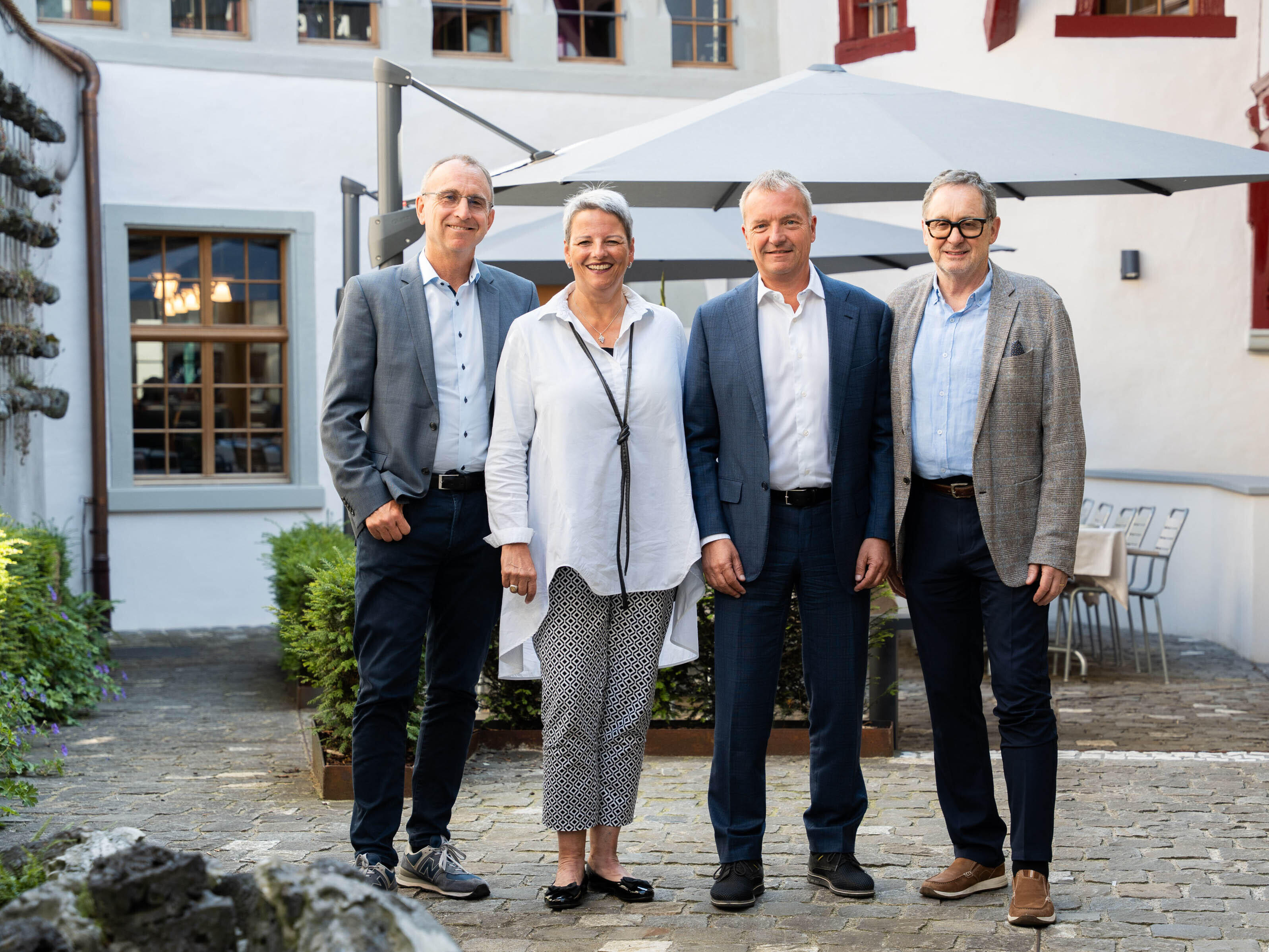 Eine Frau und drei M&auml;nner stehen im Innenhof eines historischen Geb&auml;udes.